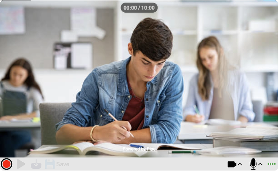 A student writes in a classroom surrounded by classmates engaged in their own work while being recorded using addpipe's recording client